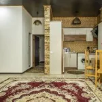 اتاق پذیرایی فرش شده به همراه آشپزخانه با کابینت های سفید واحد آپارتمان در ایزدشهر 8746538767